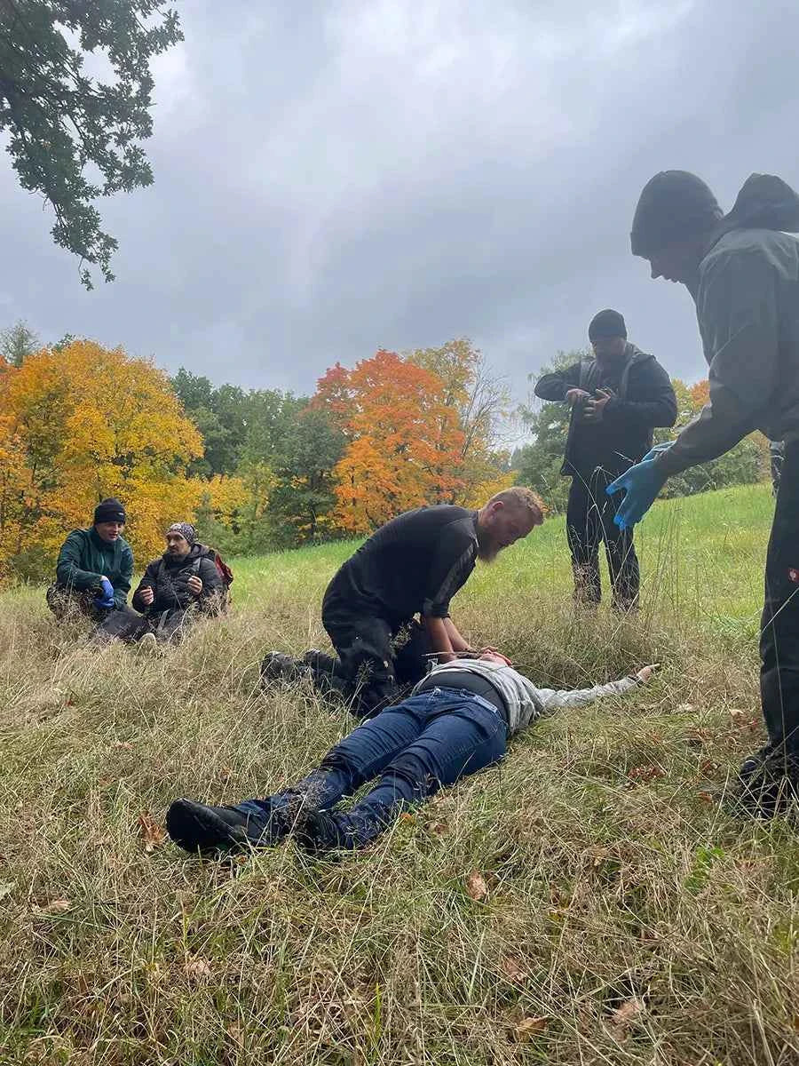 Ersthelfer untersucht eine flach am Boden liegende Person auf einer Herbstwiese bei einem Outdoor Erste-Hilfe-Kurs in Deutschland